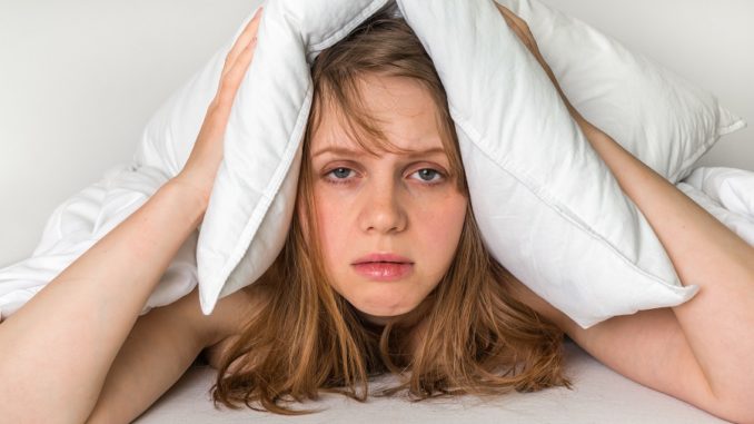 Woman in bed covering ears with pillow because of noise