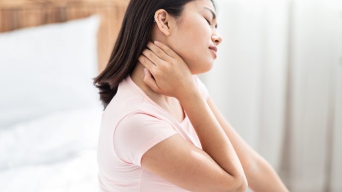 Asian Woman Massaging Aching Neck Sitting In Bed At Home